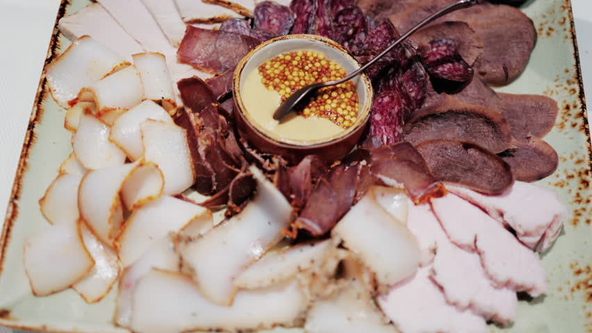Gourmet charcuterie board with assorted cured meats, smoked slices, and a mustard seed sauce served in a bowl