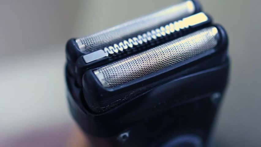 Extreme macro close-up of a modern electric shaver head, highlighting the perforated metal foil mesh texture and central cutting element for men
