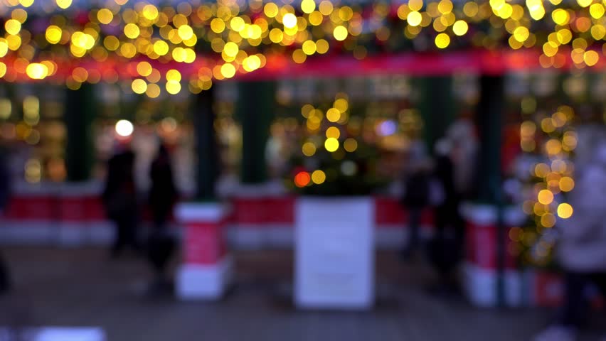 People in defocus shop gifts and souvenirs on New Years fair of evening city. Blurred christmas market with Christmas decorations.