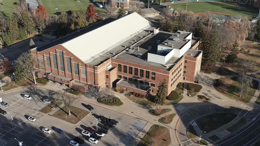 Cinematic rotating aerial shot around Jenison Fieldhouse at Michigan State University capturing the historic architecture and expansive campus grounds.