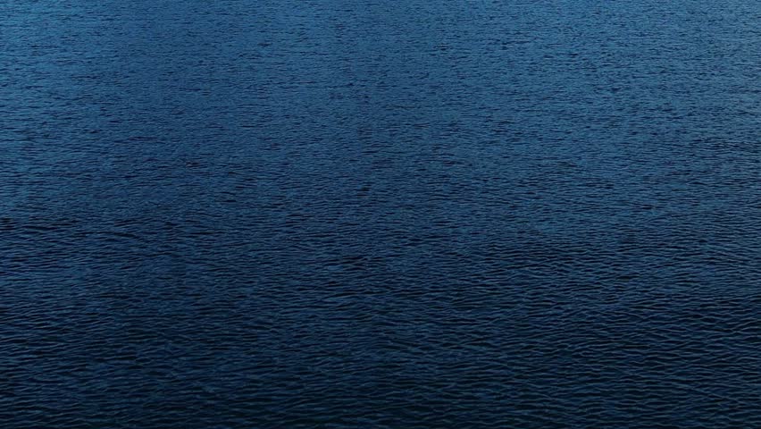 A drone captures a peaceful blue lake reflecting the surrounding Alps in Italy. The clear water contrasts beautifully with the rugged mountain terrain nearby.