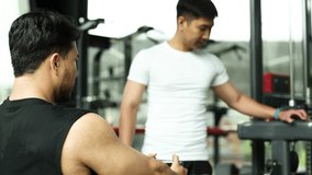 Personal trainer guides client on seated cable row machine in brightly lit Bangkok gym. - Powered by Shutterstock - Get 15% off with code: PIKWIZARD15