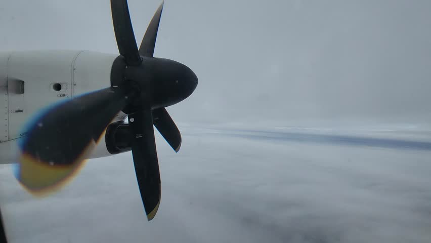 Window view of Dash 8-400 turboprop aircraft with prop spinning at cruise altitude on a cloudy winter day