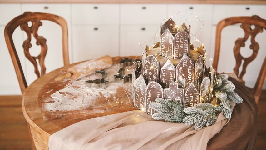Gingerbread village decorated with lights and pine branches on a table with baking tools