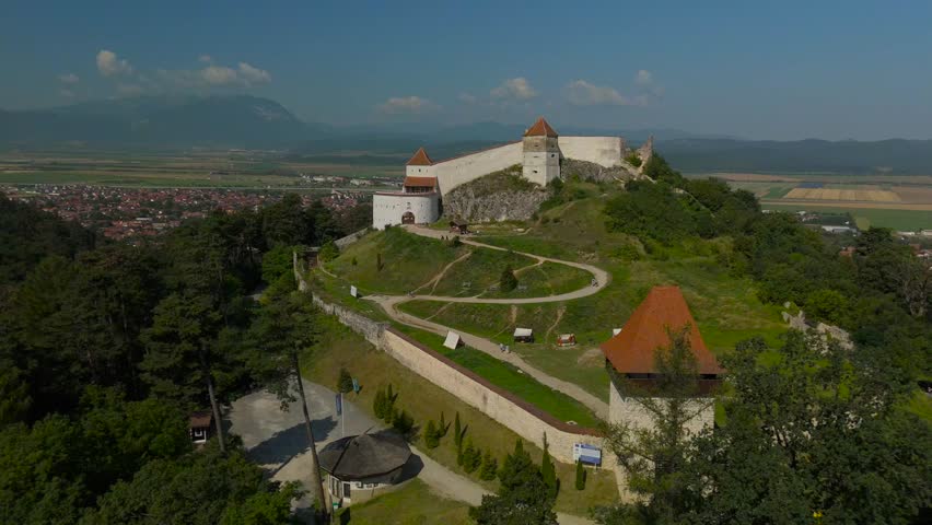 Top down aerial view of the medieval Rasnov fortress above Rasnov town and forested hill in Transylvania, Romania, on a sunny summer day