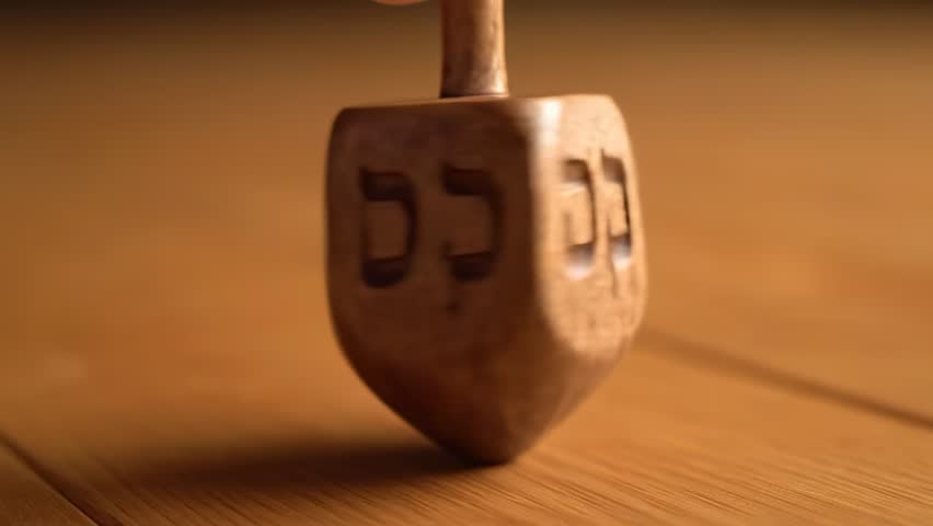Close-up shot of a traditional wooden dreidel spinning on a warm wooden surface. Perfect for Hanukkah holiday celebrations, Jewish cultural traditions, and festive content. - Powered by Shutterstock - Get 15% off with code: PIKWIZARD15