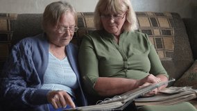 Elderly women reminiscing together. Women flipping through nostalgic photo albums. Senior ladies share memories on comfortable sofa. Two older females enjoy quiet moment flipping through photographs - Powered by Shutterstock - Get 15% off with code: PIKWIZARD15