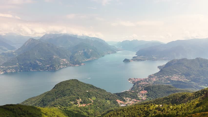Cima Monte Grona Expansive view of Lake Comos blue waters surrounded by lush mountains and charming Italian villages under a bright summer sky, showcasing the Lombardy landscape, slow drone glide