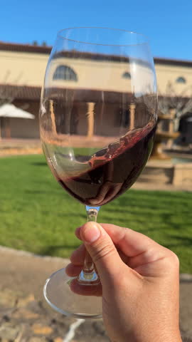 Slow motion closeup shot of a hand swirling a glass of red wine at a wine tasting in Stellenbosch, South Africa.