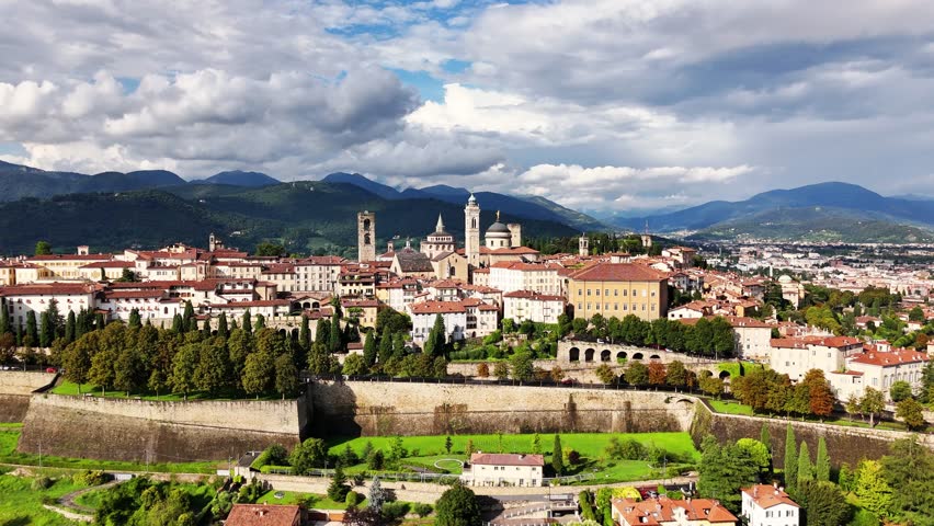 Bergamo città Alta historic center revealing landmarks, the Venetian Walls, Campanone (Civic Tower), Cathedral dome, Basilica Santa Maria Maggiore, Colleoni Chapel, and surrounding Alps, Drone push in