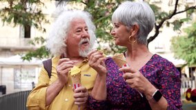 Joyful elderly couple enjoying a date outdoors, laughing and talking while eating delicious ice cream cones in a city park during a summer vacation, enjoying their active retirement lifestyle - Powered by Shutterstock - Get 15% off with code: PIKWIZARD15