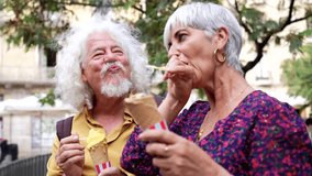 Joyful senior couple with white hair eating delicious ice cream cones in a city park, sharing a happy and sweet moment together while traveling on vacation during a warm summer day - Powered by Shutterstock - Get 15% off with code: PIKWIZARD15