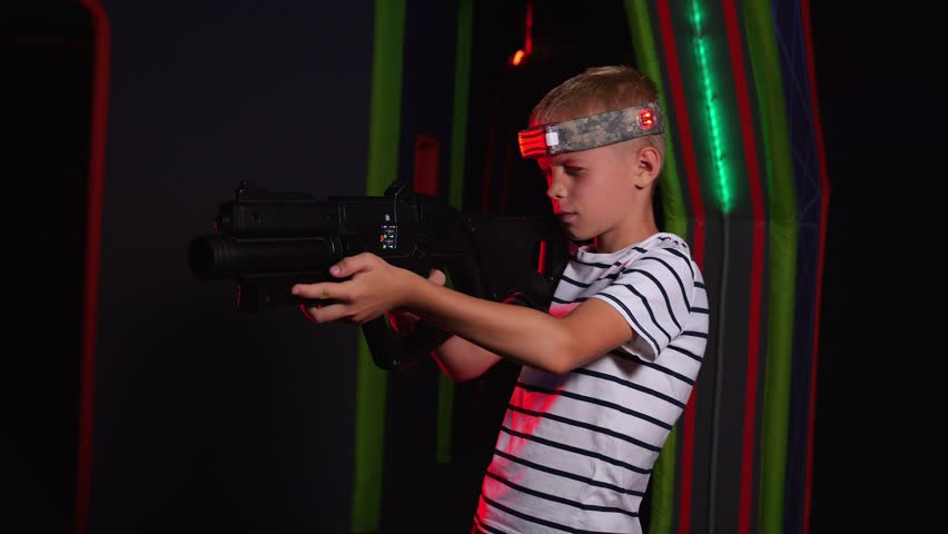 Portrait of a boy with laser guns, having fun on a dark laser tag arena. Portrait of the boy with a laser weapon in the play area. There are glowing sensors on his head.