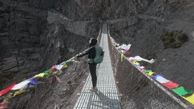 Wide Shot of Woman Hiker Crossing Mountain Suspension Bridge with Prayer Flags at Annapurna circuit trek on the way to Tilicho lake. - Powered by Shutterstock - Get 15% off with code: PIKWIZARD15