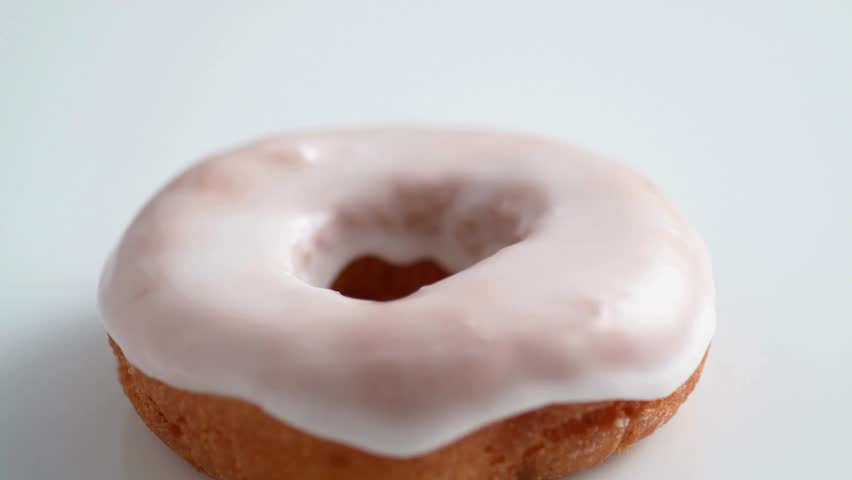 Colorful sprinkles falling onto a frosted donut. Sweet treat close-up shot. Confection is being decorated. Dessert concept. glazed donut on a white background