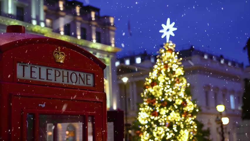 Christmas in London with a red telephone booth in front of an illuminated Christmas Tree in Central London, England, and snow falling during dusk