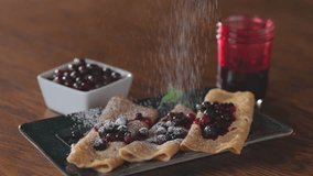 sprinkling powdered sugar on a Close-up of homemade crepes topped with fresh huckleberries, berry jam on a rustic wooden table. - Powered by Shutterstock - Get 15% off with code: PIKWIZARD15
