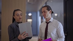 Professional business colleagues engaged in a collaborative discussion in an office hallway. They examine a tablet and notes, sharing insights and working together on a project. - Powered by Shutterstock - Get 15% off with code: PIKWIZARD15