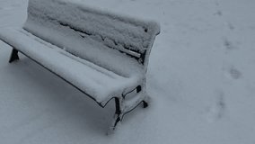 Park bench covered in thick fresh snow during cold winter day with visible footprints in background - Powered by Shutterstock - Get 15% off with code: PIKWIZARD15