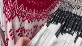 Close-up of a hand holding a red and white knitted Christmas sweater with Nordic pattern in a clothing store during holiday shopping season - Powered by Shutterstock - Get 15% off with code: PIKWIZARD15