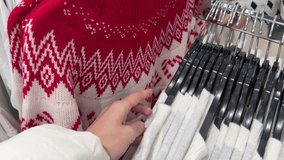 Close-up of a hand holding a red and white knitted Christmas sweater with Nordic pattern in a clothing store during holiday shopping season - Powered by Shutterstock - Get 15% off with code: PIKWIZARD15