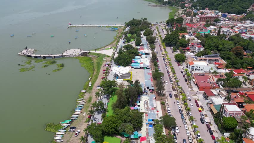 Drone footage capturing the scenic Lake Chapala, its vibrant malecon, and bustling lakeside town in Jalisco, Mexico, on a bright sunny day.