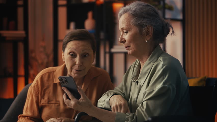 Two smiling senior women friends discussing shopping deals in online store