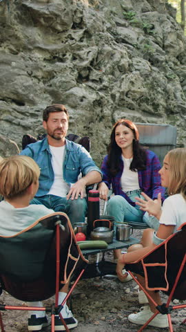 Happy family including mother, father, and two kids enjoying summer holidays in the garden or park. Smiling parents and children are spending leisure time together having picnic outdoor in forest near