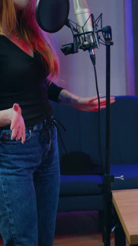 Adorable successful 25-aged seductive woman standing in front of recording equipment and singing while her experienced stylish male partner playing on the guitar during recording joint song in home