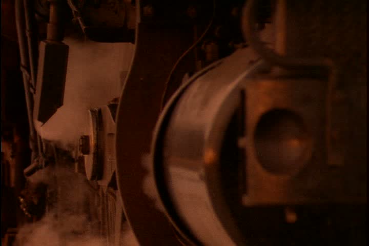 Mid Continent Railway, New Freedom, Wisconsin. CU sidelong view of big rusty wheels of 1885 steam train. Puffs of steam surround wheel. Clip has great sound of steam hiss and ringing train bell.