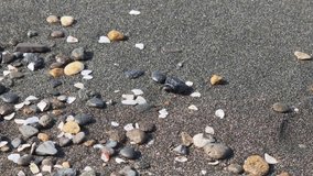 The encroaching ocean tide is gradually engulfing a shadowy volcanic sand beach adorned with tiny pebbles and shells. An up close perspective captures the soft waves gently caressing the shore - Powered by Shutterstock - Get 15% off with code: PIKWIZARD15