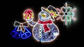 Illuminated LED Christmas decoration featuring a glowing snowman with a gift box, bells, and a snowflake on a brick wall background at night. - Powered by Shutterstock - Get 15% off with code: PIKWIZARD15