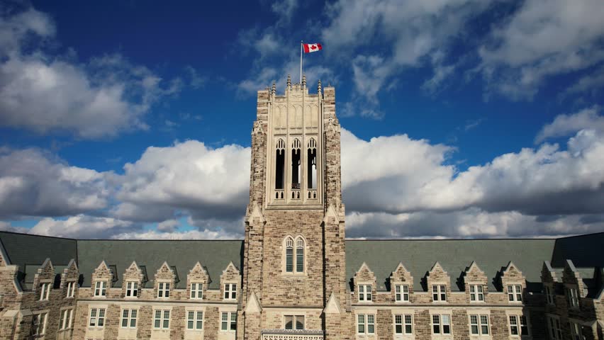 Aerial view of classic collegiate stone tower with Canadian flag and dramatic clouds