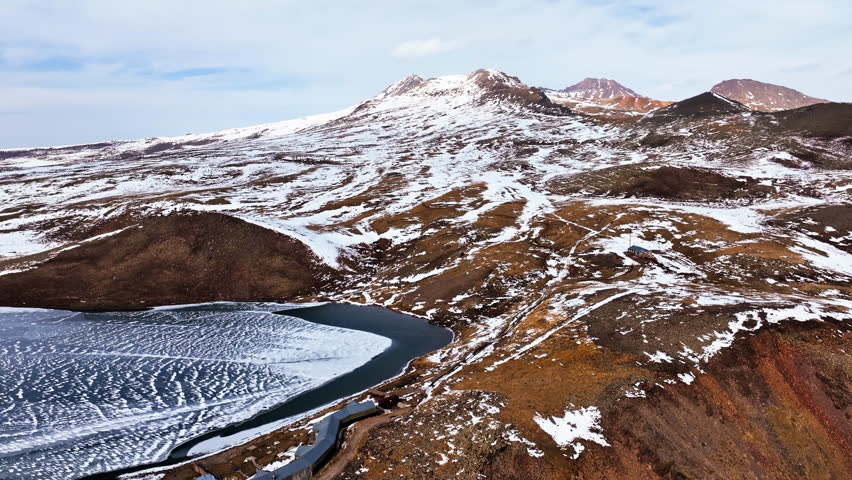 A snowy mountain range with a lake in the foreground. The lake is frozen and the snow is covering the ground