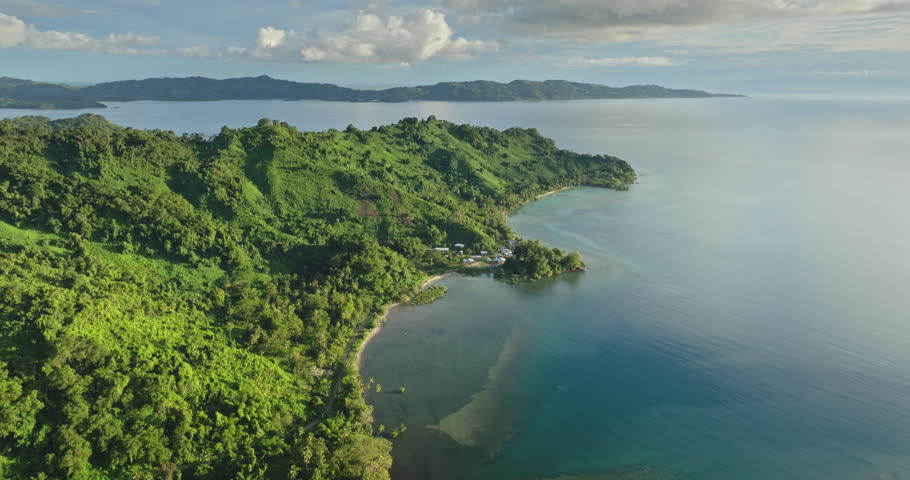 Lush green jungle hills meet the tranquil blue ocean along Vanua Levu Savusavu coastline, under a partly cloudy sky pristine tropical paradise seen from above