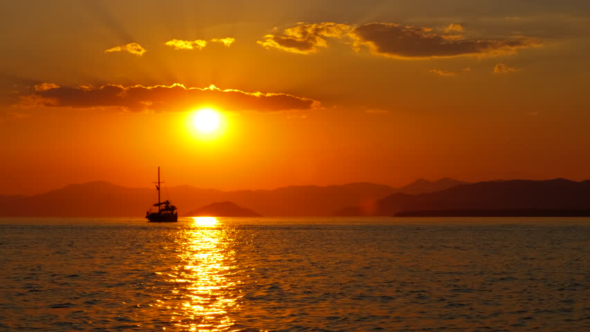 Touristic ship floating during dusk. A view of touristic ship silhouette on river waves against orange horizon