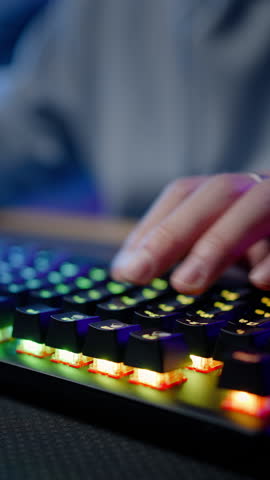 Details on computer keyboard with colorful lights and hands of a gamer streamer playing online video game, streaming virtual game on dark interior. People. Technology and digital entertainment concept