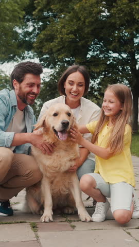 Happy family rejoices stroking dog and spending time on Sunday walk. Positive parents and daughter touch fluffy pet in city park concept slow motion