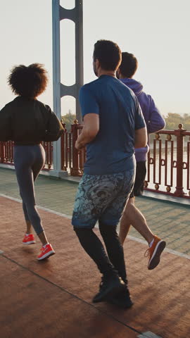 Group of diverse young people running on sports path on bridge early in morning, slow motion