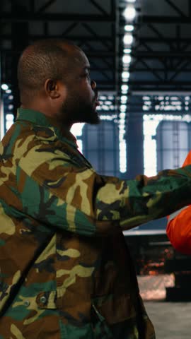 Vertical Video Worker and military officer in manufacturing plant converted for wartime industry, coordinating tools for defense production. Facility shifts operations toward weapons supply