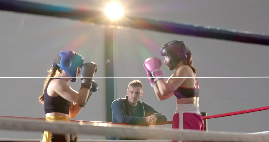 Two female boxers sparring with jabs, hooks in boxing ring, waveform spiking, coach watching. Fighters, women, gloves, headgear, gym, lensflare, combat