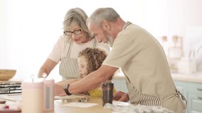 Loving grandparents teaching their adorable curly-haired granddaughter how to roll dough for baking cookies in a bright, modern kitchen - Powered by Shutterstock - Get 15% off with code: PIKWIZARD15