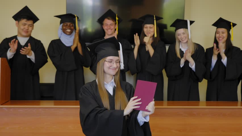 Young Caucasian woman holding diploma while classmates applaud her. 