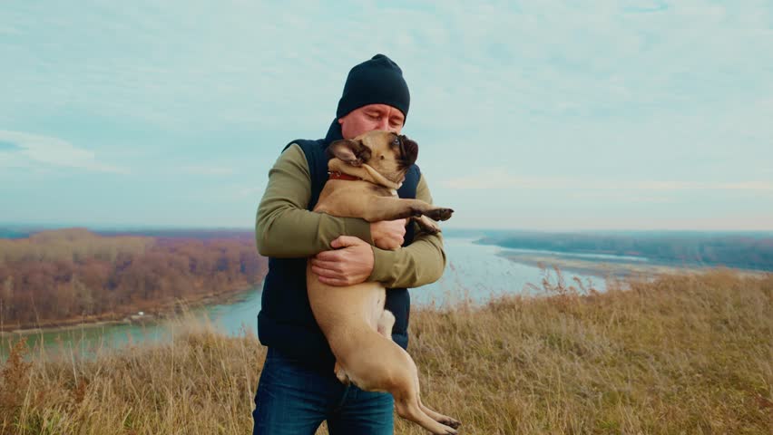 A Heartwarming Moment of Connection Between a Man and His Beloved Dog at an Expansive Natural Landscape with a Calm River in the Background, Captured in Two Frames of Joyful Bonding.