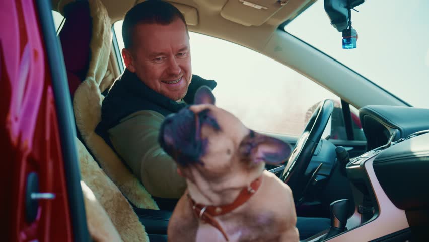 A Joyful Moment: A Man and His Playful Dog Enjoy Quality Time Together Inside a Car, Capturing the Essence of Friendship and Affection Between Human and Pet in a Cozy Setting