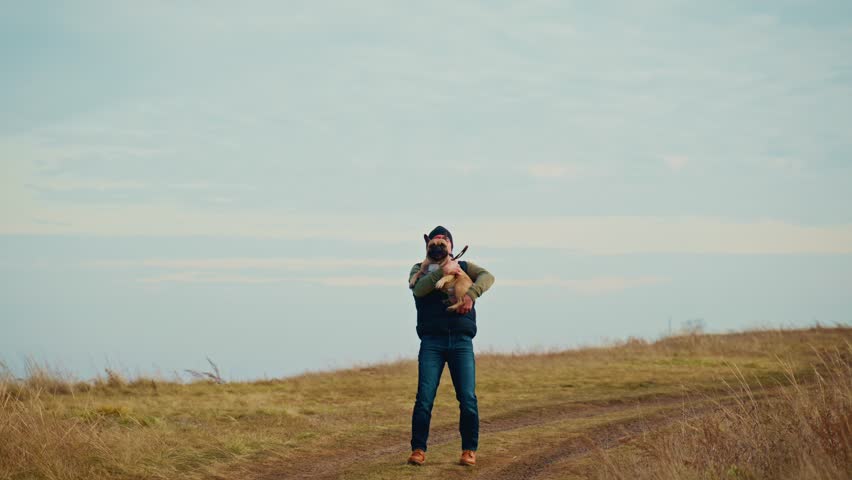 A man stands proudly on a scenic hillside holding a dog close, capturing a moment of companionship and outdoor life. The beautiful landscape around them enhances the bond between human and pet.