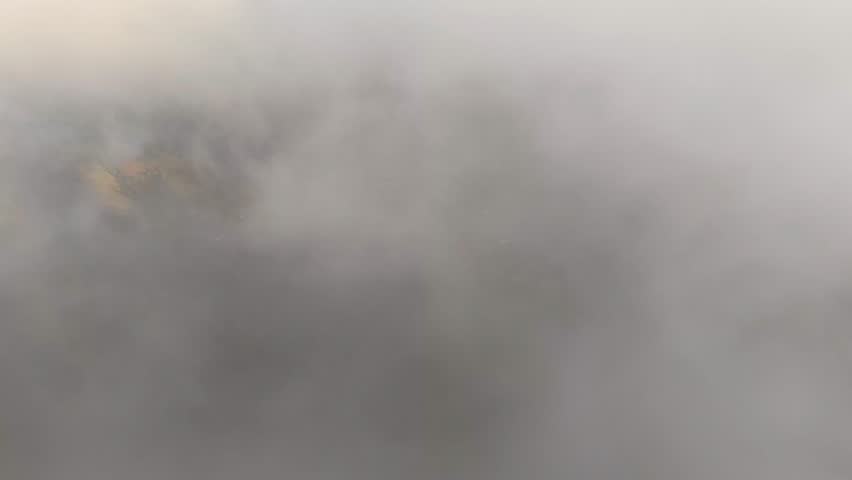 High drone shot moving forward through dark clouds and revealing the rural Zacatlán valley below, with fields, scattered houses, forest areas and a winding road.