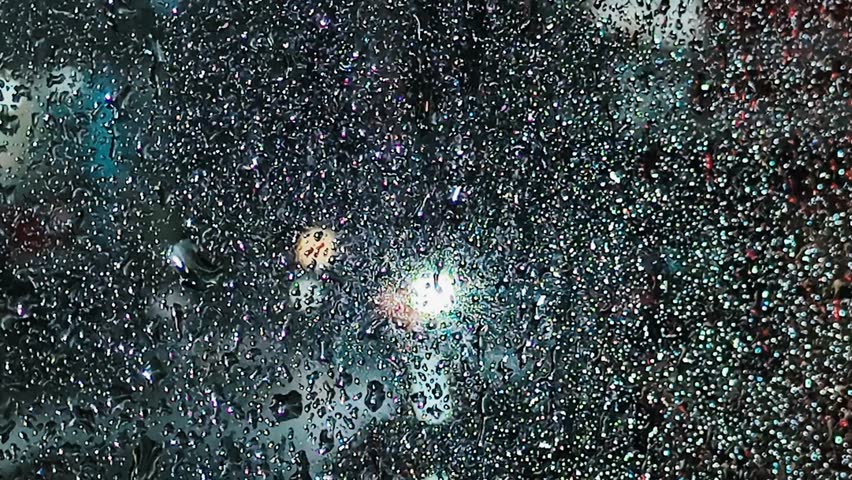 Close up of water droplets on glass with blurred city lights in the background. A moody and atmospheric shot of a rainy night in the city.