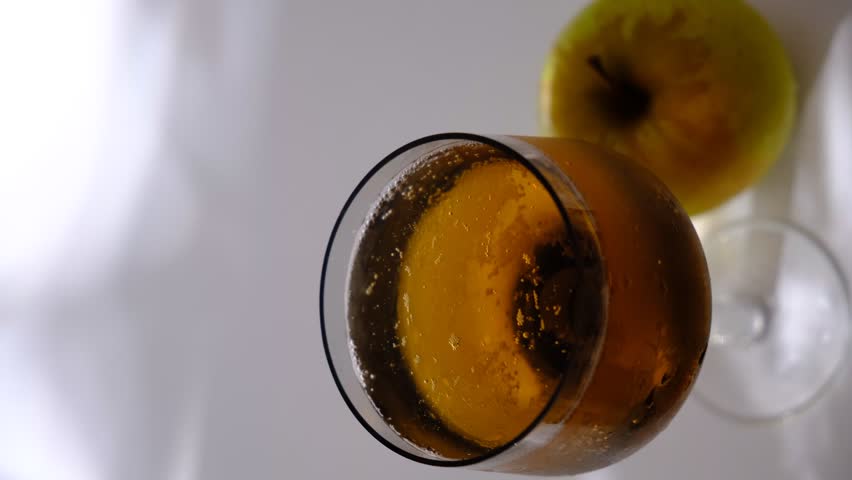 Glass of brut apple cider from Normandy. White table with casting shadows and sunlight. Ripe yellow fruits on the table. Atmospheric mood.	