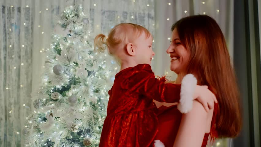mother embraces child near christmas tree, caucasian mom standing with her infant by decorated pine, gentle glow surrounds mother lovingly holding her baby close